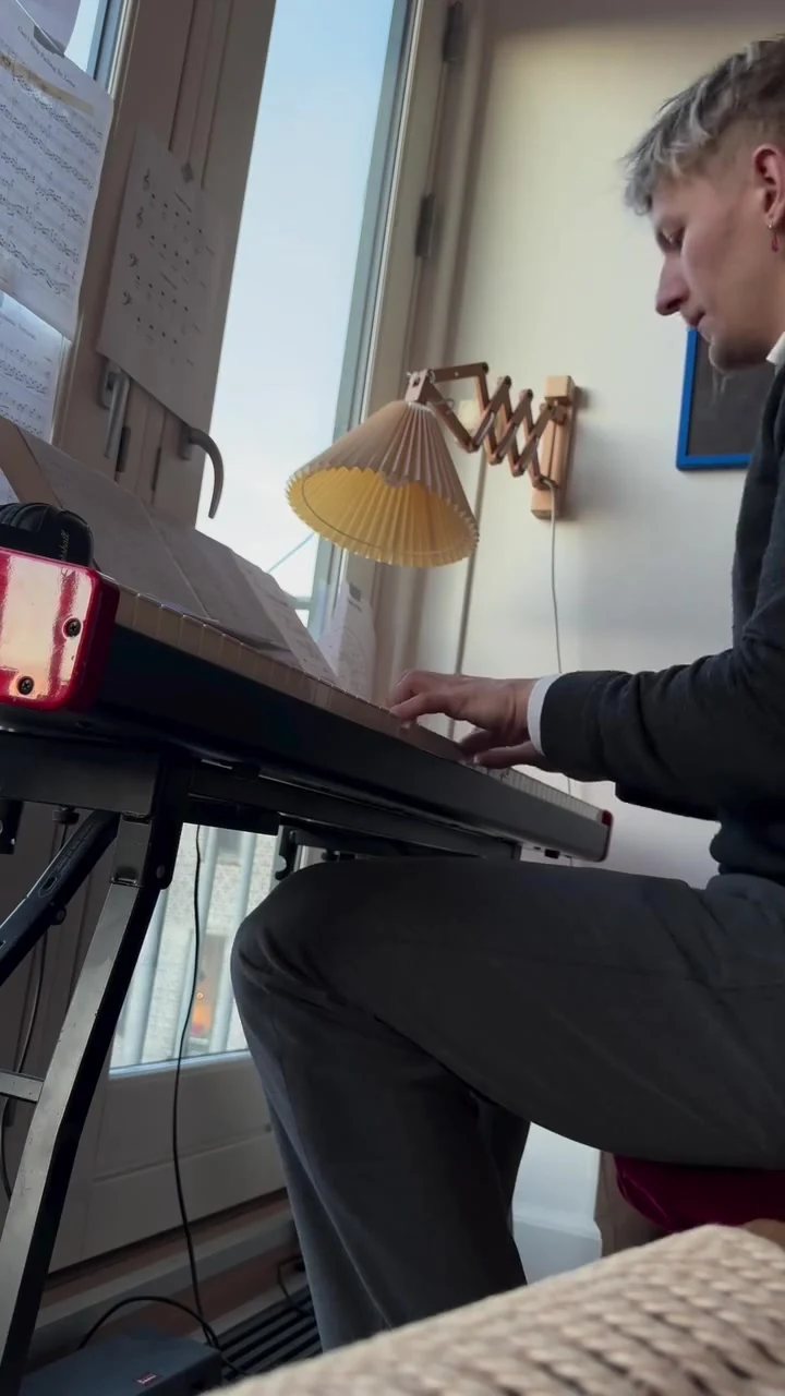 Beyorn spiller keyboard ved vinduet med noder og en plisseret lampe.